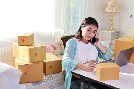 Attractive happy asian pregnant woman sitting and using mobile smart phone and writing order for customer with tablet. Expectant mother preparing and working for baby birth during pregnancy concept.の写真素材