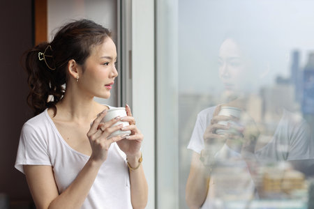 Portrait of confident and beauty young asian businesswoman with coffee cup standing and looking away in modern hotel with city blurred background. Success business and lifestyle conceptの写真素材
