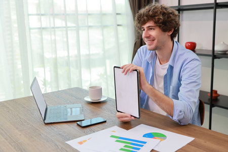 Caucasian businessman online meeting with colleage or customer and showing something on white screen tablet while sitting at home and workingの写真素材