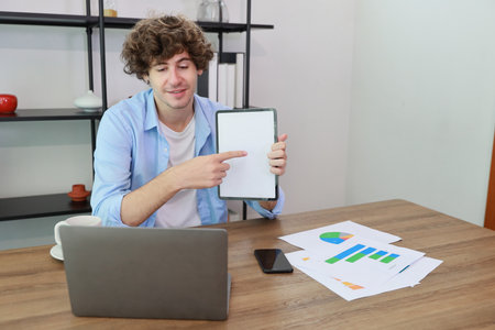 Caucasian businessman online meeting with colleage or customer and showing something on white screen tablet while sitting at home and workingの写真素材