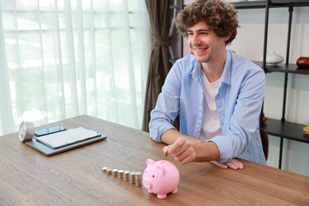 Caucasian businessman putting coin into piggy bank with saving growth on stacking coin growing, meaning of earning money or investment or financial or tax for business advertising conceptの写真素材