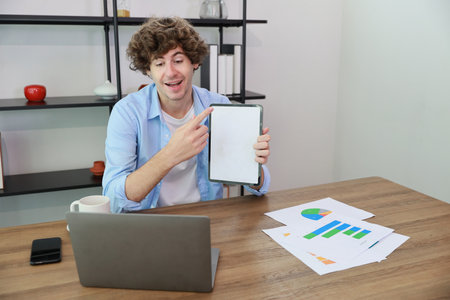 Caucasian businessman online meeting with colleage or customer and showing something on white screen tablet while sitting at home and workingの写真素材