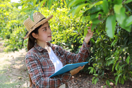Asian agronomist or woman farmer reading report and inspecting growing crops data from clipboard for increasing productivity in agriculture field, modern smart farming with technology conceptの写真素材