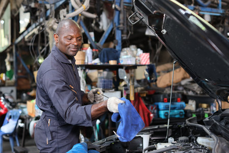 Man technician car mechanic in uniform checking maintenance a car service at repair garage station. Worker checking motor oilÂ level in car engine. Concept of car center repair service.の写真素材