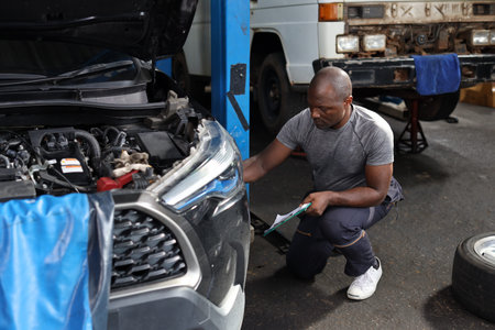 Man technician car mechanic in half uniform with clipboard and checking maintenance broken car while...