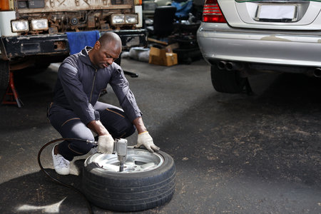 Man technician car mechanic in full uniform holding tire for replacement or changeing at repair garage. Happy asian worker smiling and looking at camera. Concept of car center repair service.の写真素材