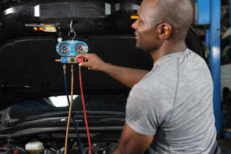 Rear view mechanic hands in half uniform checking car air conditioning system refrigerant recharge, leak detection, fill refrigerant service. Concept of car center repair service.の写真素材