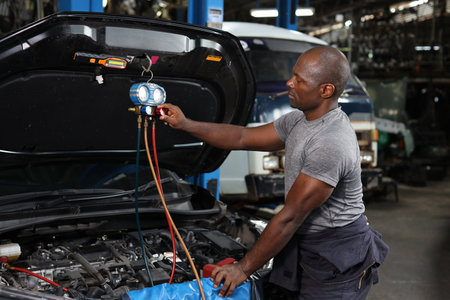 Mechanic in half uniform checking car air conditioning system refrigerant recharge, leak detection, fill refrigerant service. Concept of car center repair service.の写真素材