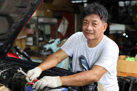 Man technician car mechanic in half uniform checking maintenance a car service at repair garage station. Worker holding wrench and fixing breakdown vehicle. Concept of car center repair service.の写真素材