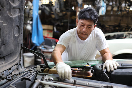Man technician car mechanic in half uniform checking maintenance a car service at repair garage station. Worker holding wrench and fixing breakdown vehicle. Concept of car center repair service.の写真素材