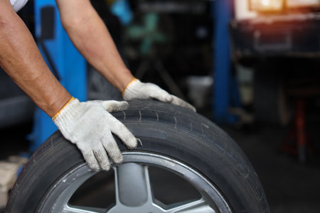 Man technician car mechanic hands in uniform holding tire for replacement or changeing at repair garage. Concept of car center repair service.の写真素材