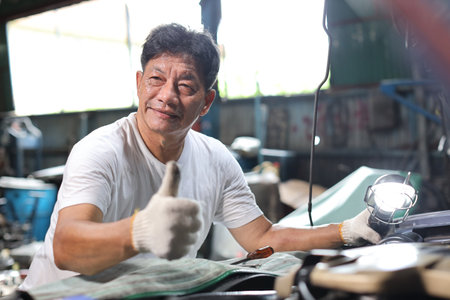 Asian technician engineer or worker standing and holding wrench and showing thumb up celebrate successful or completed task or deal commitment at heavy industry manufacturing factoryの写真素材