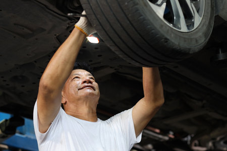 Man technician car mechanic in half uniform checking maintenance a lifted car service at repair garage station. Worker holding wrench and fixing breakdown vehicle. Concept of car center repair serviceの写真素材