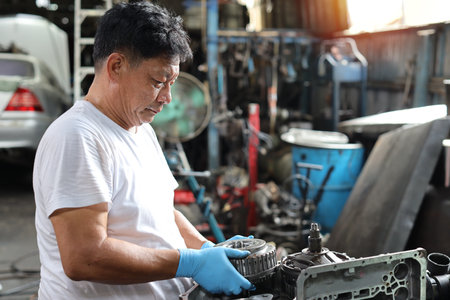 Man technician car mechanic in half uniform checking maintenance a car service at repair garage station. Worker holding wrench and fixing breakdown vehicle. Concept of car center repair service.の写真素材