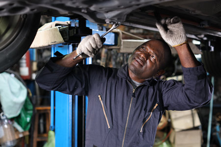 Man technician car mechanic in uniform checking maintenance a lifted car service at repair garage station. Worker using flashlight and wrench fixing breakdown vehicle. Car repair service concept.の写真素材