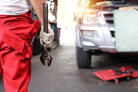Rear view technician engineer or worker man hand in half uniform standing and holding wrench checking maintenance a car service at repair garage station. Concept of car center repair service.の写真素材
