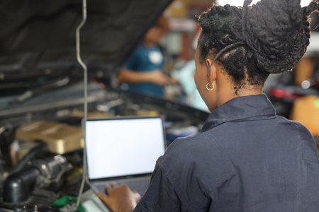 Rear view woman technician car mechanic in uniform checking maintenance a car service with computer at repair garage station. Car repair service conceptの写真素材