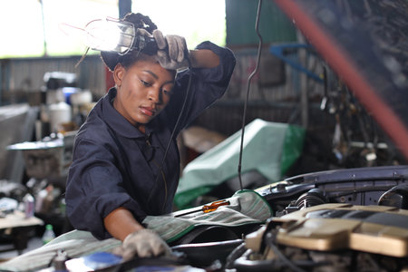 Technician car mechanic in uniform checking car service at repair garage station. Worker woman holding flashlight and wipe the sweat away while fixing breakdown vehicle. Concept of car repair service.の写真素材
