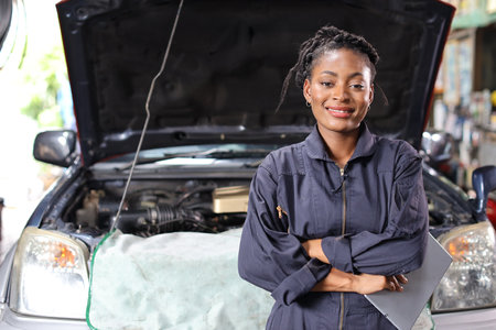 Woman technician car mechanic in uniform checking maintenance a car service with tablet while crossed arms at camera and smile at repair garage station. Car repair service conceptの写真素材