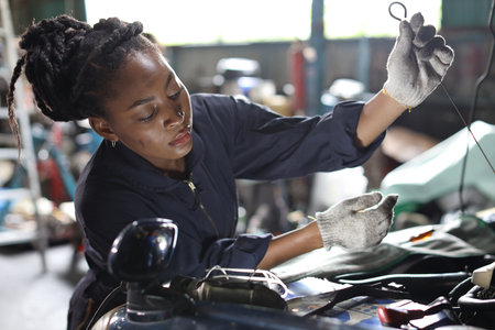 Woman technician car mechanic in uniform checking maintenance a car service at repair garage station. Worker checking motor oilÂ level in car engine. Concept of car center repair service.の写真素材