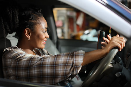 Portrait of happy afirican woman with smiling face driving car vehicle while using smart mobile phone on the road outdoorの写真素材