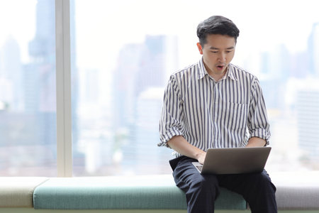 Young asian business man sitting and using computer in business office building and city backgroundの写真素材