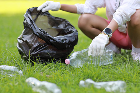 Young beautiful asian volunteer woman hands holding garbage bag and picking up litter while cleaning...