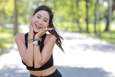 Young cheerful asian transgender LGBT in sportswear with earphone and wristband standing while her hands touching her cheeks with happy smiling face and looking at camera. pride and equality concept.の写真素材