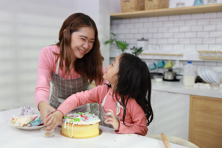 Happy lovely asian single mom and cute daughter in apron having fun with teaching and decorating homemade cake in the kitchen. Family lifestyle cooking with education concept.の写真素材