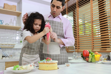 Happy lovely asian single dad and cute daughter in apron having fun with teaching and decorating homemade cake in the kitchen. Family lifestyle cooking with education concept.の写真素材