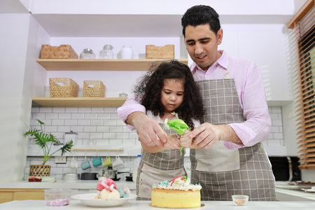 Happy lovely asian single dad and cute daughter in apron having fun with teaching and decorating homemade cake in the kitchen. Family lifestyle cooking with education concept.の写真素材
