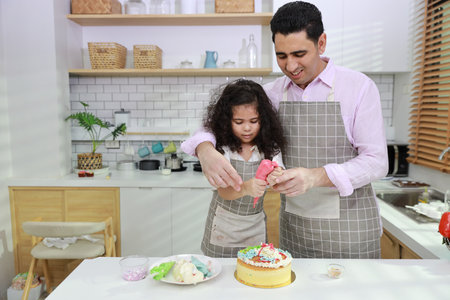 Happy lovely asian single dad and cute daughter in apron having fun with teaching and decorating homemade cake in the kitchen. Family lifestyle cooking with education concept.の写真素材
