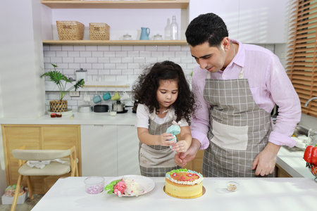 Happy lovely asian single dad and cute daughter in apron having fun with teaching and decorating homemade cake in the kitchen. Family lifestyle cooking with education concept.の写真素材