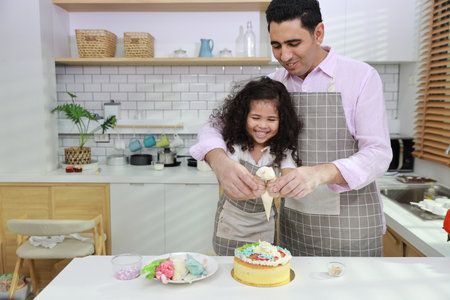 Happy lovely asian single dad and cute daughter in apron having fun with teaching and decorating homemade cake in the kitchen. Family lifestyle cooking with education concept.の写真素材