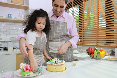 Happy lovely asian single dad and cute daughter in apron having fun with teaching and decorating homemade cake in the kitchen. Family lifestyle cooking with education concept.の写真素材