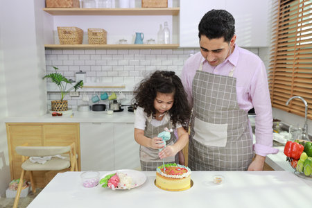 Happy lovely asian single dad and cute daughter in apron having fun with teaching and decorating homemade cake in the kitchen. Family lifestyle cooking with education concept.の写真素材