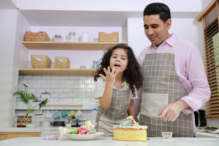 Happy lovely asian single dad and cute daughter in apron having fun with teaching and decorating homemade cake in the kitchen. Family lifestyle cooking with education concept.の写真素材