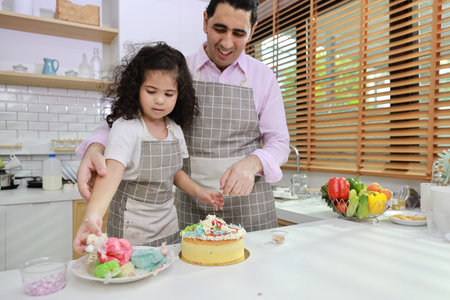 Happy lovely asian single dad and cute daughter in apron having fun with teaching and decorating homemade cake in the kitchen. Family lifestyle cooking with education concept.の写真素材