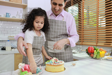 Happy lovely asian single dad and cute daughter in apron having fun with teaching and decorating homemade cake in the kitchen. Family lifestyle cooking with education concept.の写真素材