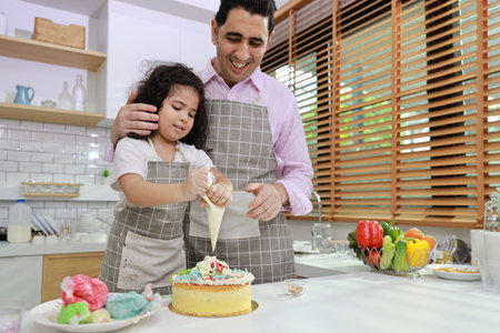 Happy lovely asian single dad and cute daughter in apron having fun with teaching and decorating homemade cake in the kitchen. Family lifestyle cooking with education concept.の写真素材