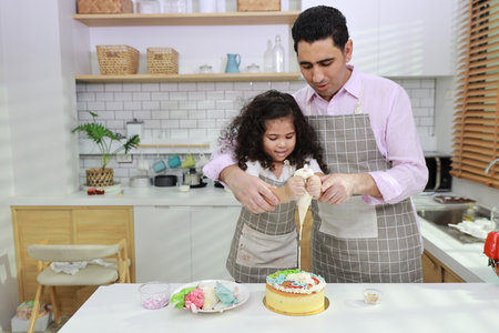 Happy lovely asian single dad and cute daughter in apron having fun with teaching and decorating homemade cake in the kitchen. Family lifestyle cooking with education concept.の写真素材