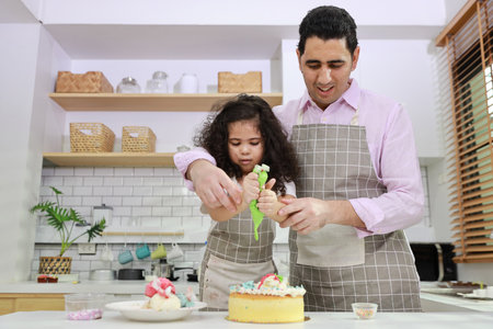 Happy lovely asian single dad and cute daughter in apron having fun with teaching and decorating homemade cake in the kitchen. Family lifestyle cooking with education concept.の写真素材