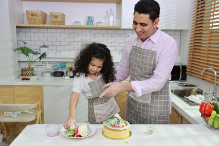Happy lovely asian single dad and cute daughter in apron having fun with teaching and decorating homemade cake in the kitchen. Family lifestyle cooking with education concept.の写真素材