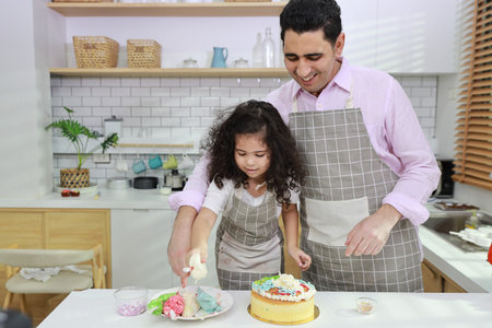 Happy lovely asian single dad and cute daughter in apron having fun with teaching and decorating homemade cake in the kitchen. Family lifestyle cooking with education concept.の写真素材