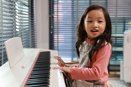 Kid asian black hair girl and hispanic currly hair girl sitting and playing piano in living room house indoor. Musical and relaxation makes them happiness. Health care lifestyle concept.の写真素材