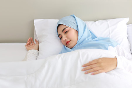 Oversleeping asian woman wearing white muslim sleepwear lying on bed with happiness.Top view portrait young cute girl sleeping in bedroom with happy and beauty face. Lifestyle conceptの写真素材