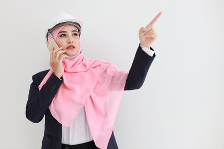 Smart young asian woman wearing blue muslim suit smiling confident, pointing and using mobile phone in studio. Isolated white background portrait with beautiful face girl. Advertisement concept.の写真素材