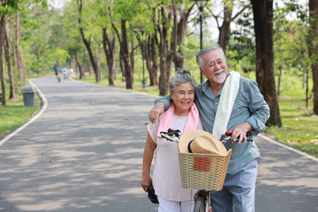 Portrait of happy asian senior man and woman walking and hugging with bicycle and binoculars in summer garden outdoor. Lover couple going to picnic at the park. Happiness marriage lifestyle concept.の写真素材