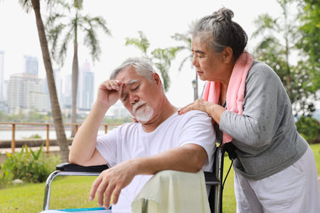 Asian senior woman or caregiver helping and consoling senior man walk with wheelchair at park...