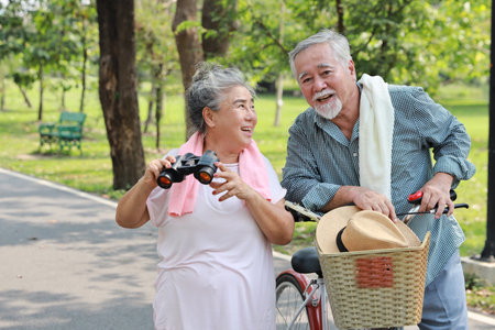 Portrait of happy asian senior man and woman walking and hugging with bicycle and binoculars in summer garden outdoor. Lover couple going to picnic at the park. Happiness marriage lifestyle concept.の写真素材